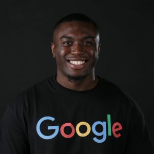 Van Dennis is an African American man wearing a black t-shirt that says Google on it. He looks directly at the camera and smiles.
